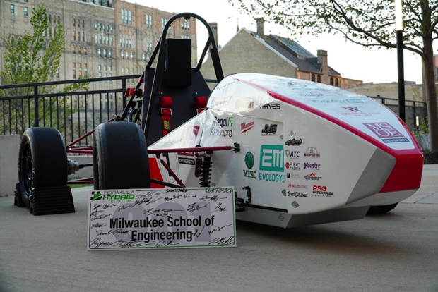 The completed Mozee Motorsports hybrid race car parked on the MSOE campus behind a signed Formula Hybrid sign reading Milwaukee School of Engineering